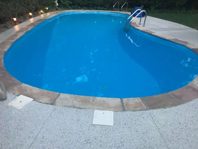Restored pool deck with stone-look coping around an in-ground pool